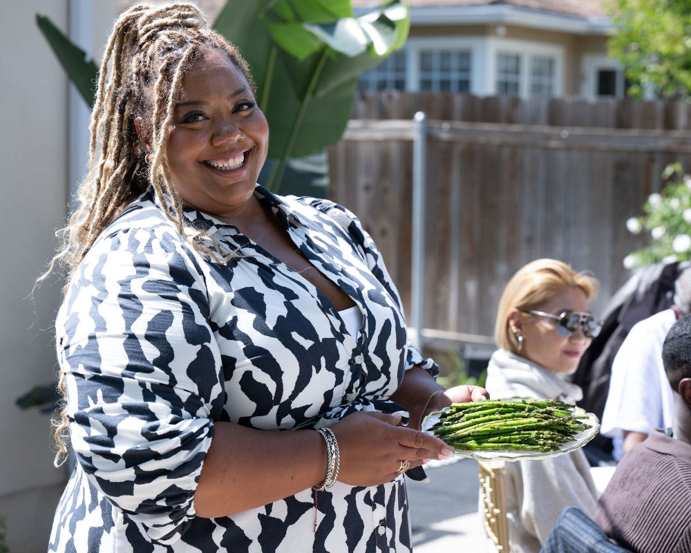 Chef Camille holding a plate of food outdoors with people and greenery in the background